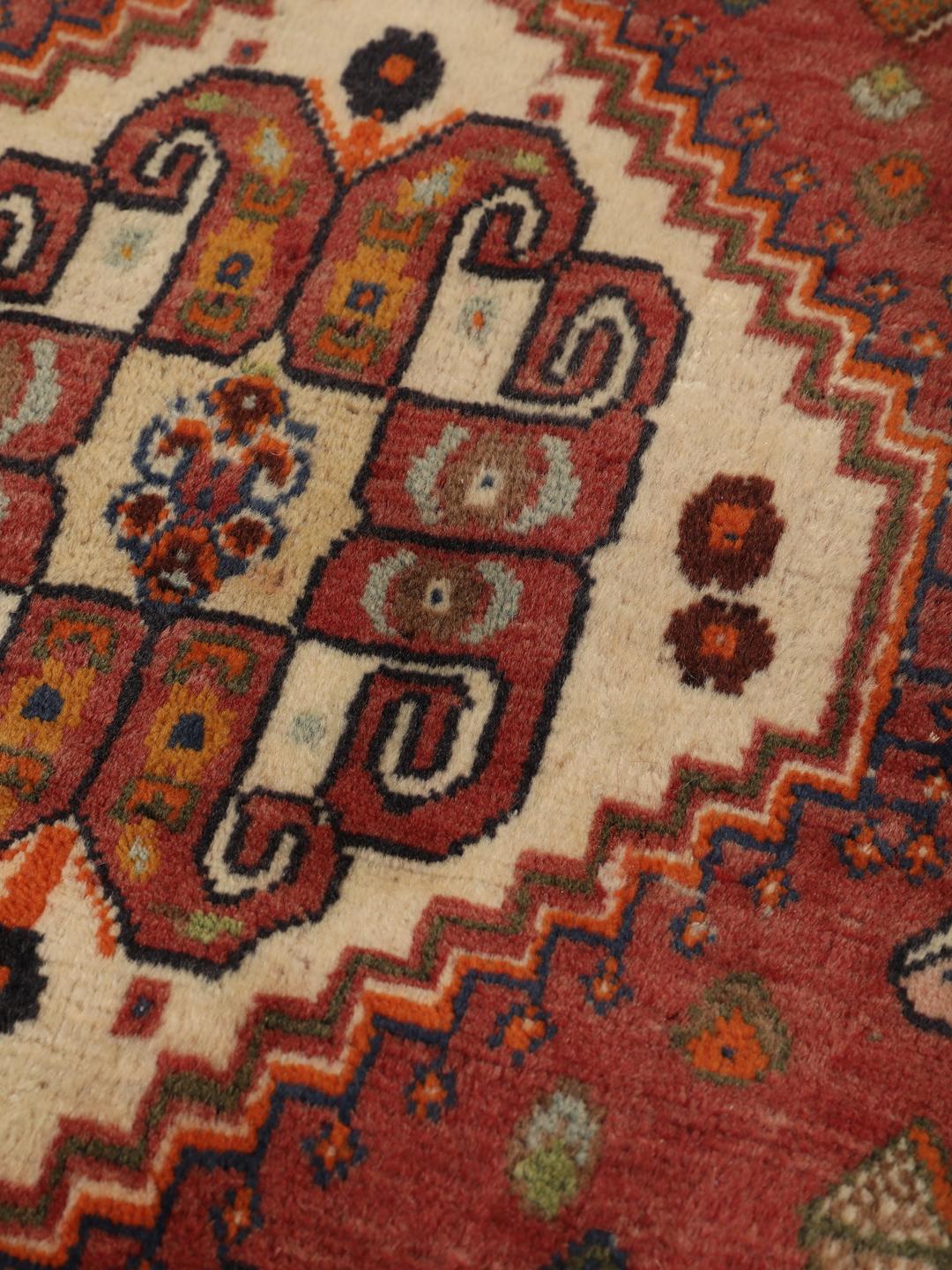 A hand-knotted, one-of-a-kind Qashqai runner rug with a deep red field and intricate geometric medallions.