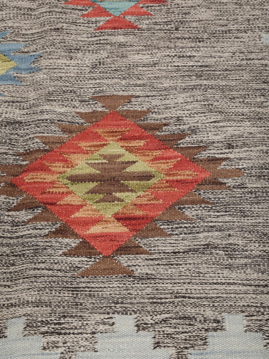 Tapete kilim indiano tecido à mão com padrões de diamante vibrantes sobre um fundo cinzento