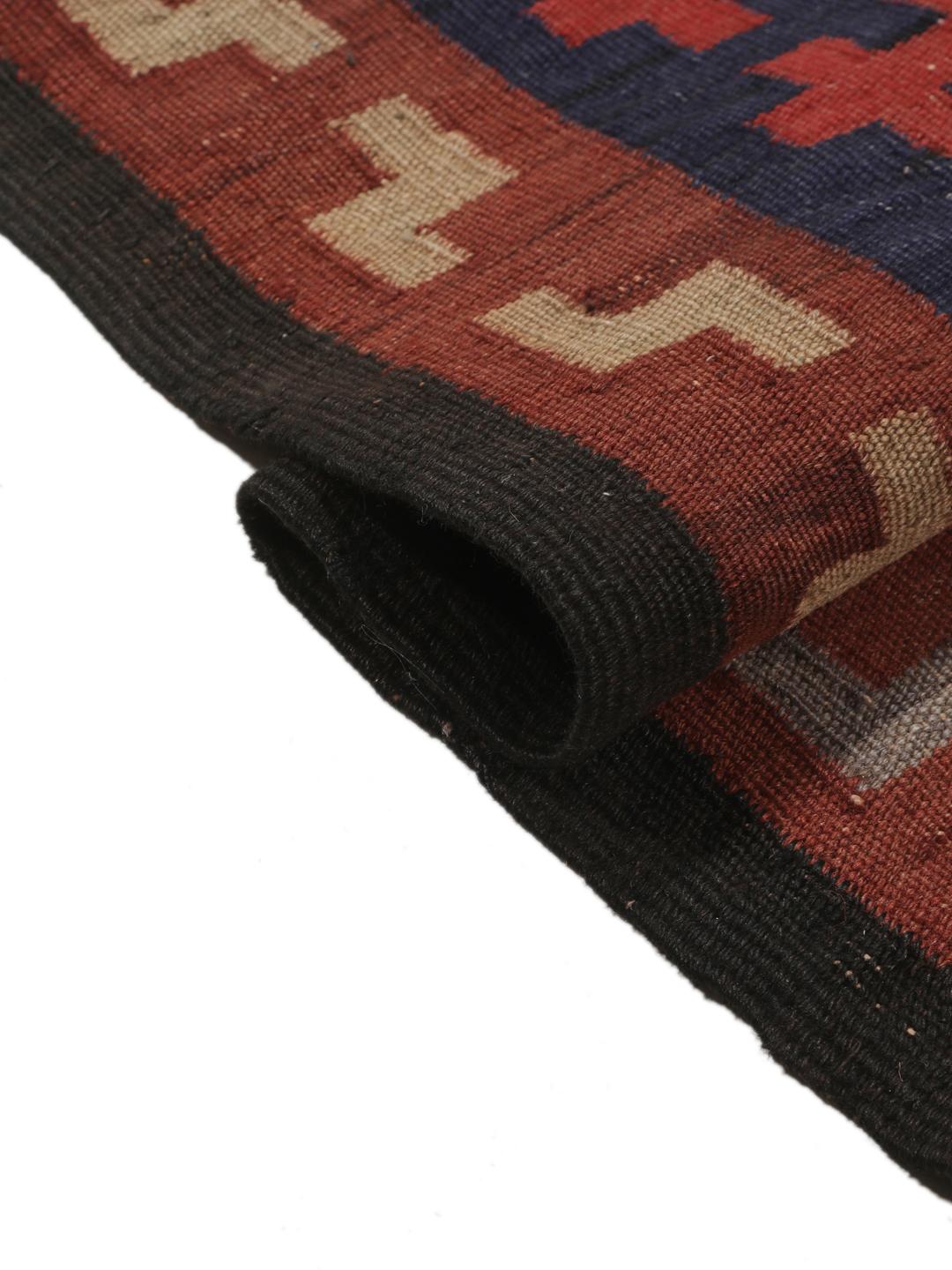 Tapis Kilim vintage afghan avec des motifs géométriques en losange dans des tons rouges et sombres.