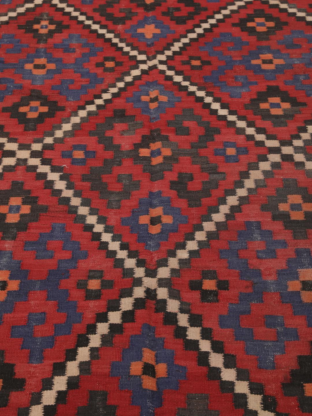 Un long tapis couloir afghan tissé à la main présentant un motif répétitif en losange dans des tons de rouge, bleu et noir.