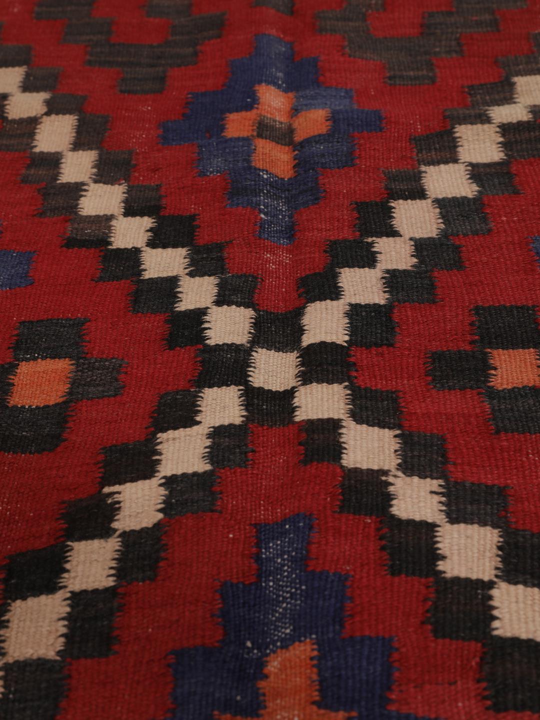 Un long tapis couloir afghan tissé à la main présentant un motif répétitif en losange dans des tons de rouge, bleu et noir.