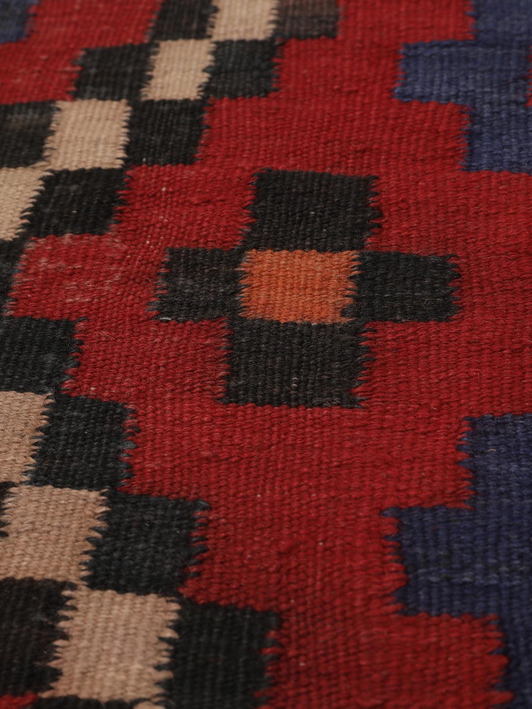 Un long tapis couloir afghan tissé à la main présentant un motif répétitif en losange dans des tons de rouge, bleu et noir.