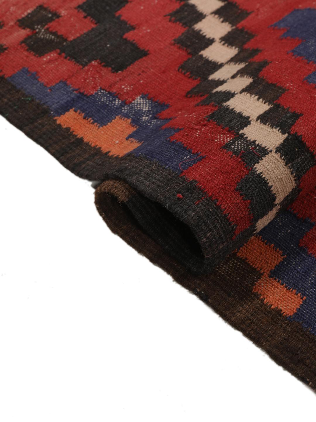 Un long tapis couloir afghan tissé à la main présentant un motif répétitif en losange dans des tons de rouge, bleu et noir.