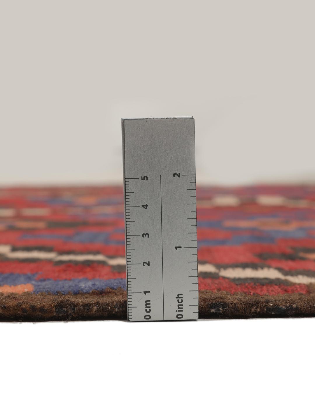 Un long tapis couloir afghan tissé à la main présentant un motif répétitif en losange dans des tons de rouge, bleu et noir.