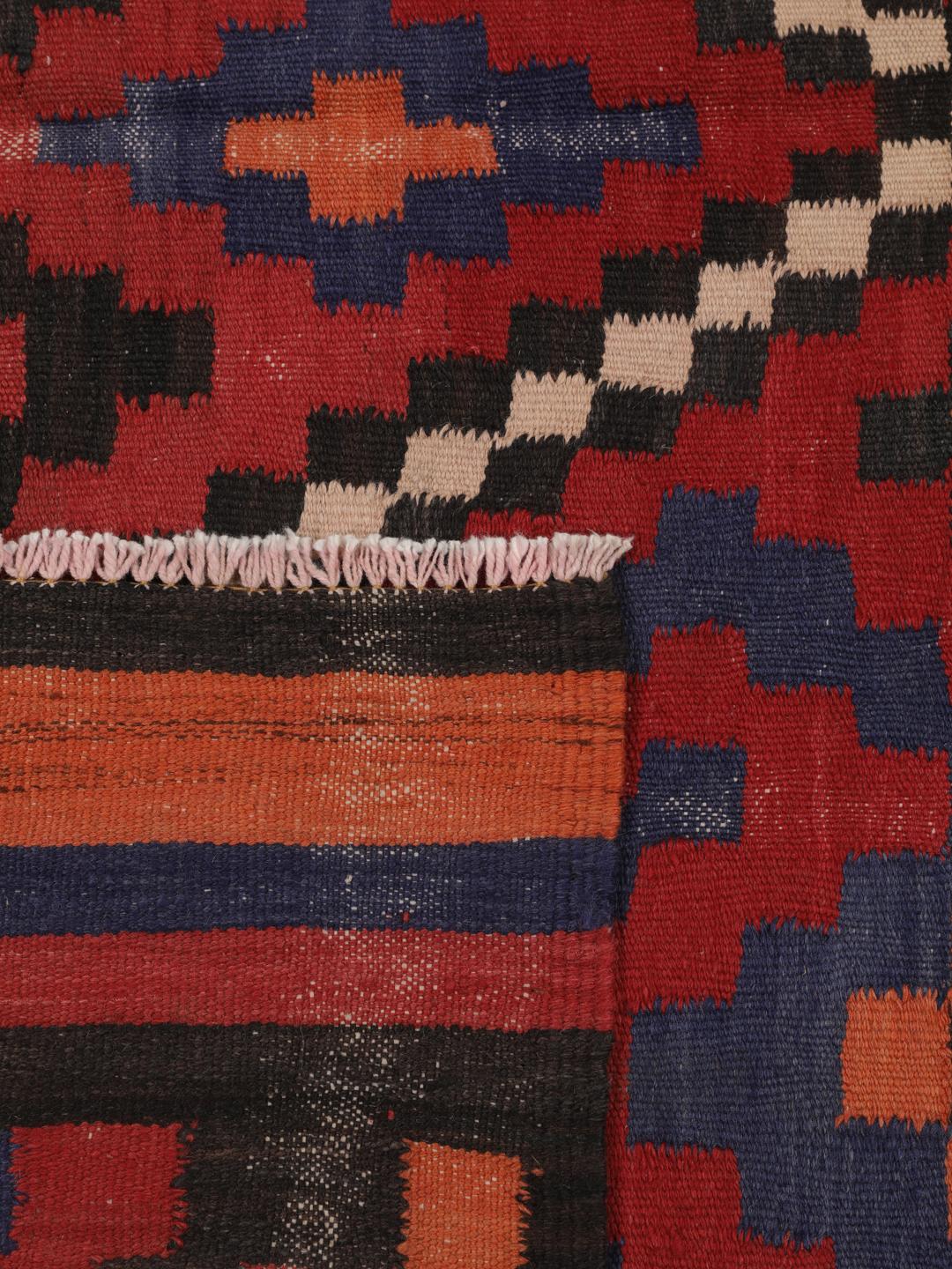 Un long tapis couloir afghan tissé à la main présentant un motif répétitif en losange dans des tons de rouge, bleu et noir.