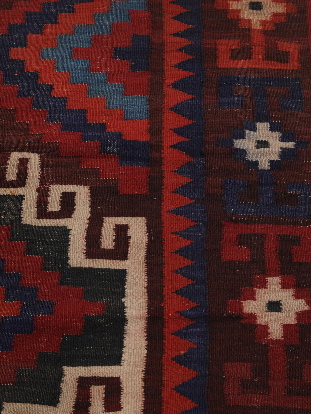 Tapis Kelim afghan tissé à la main avec des motifs géométriques en losange dans les tons rouge, bleu et noir.