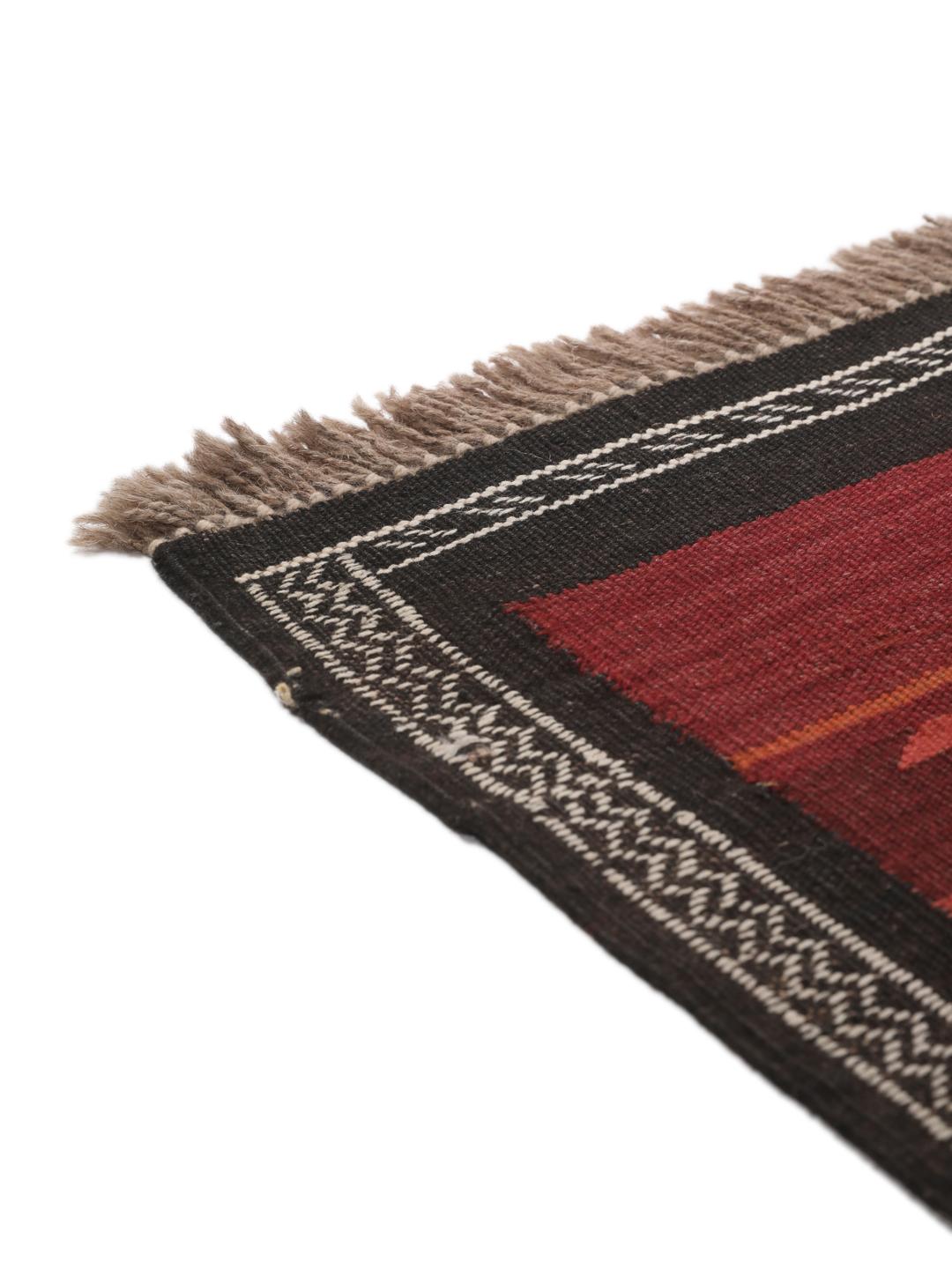 Tapis kelim afghan tissé à la main avec des motifs géométriques dans des tons rouges et sombres.