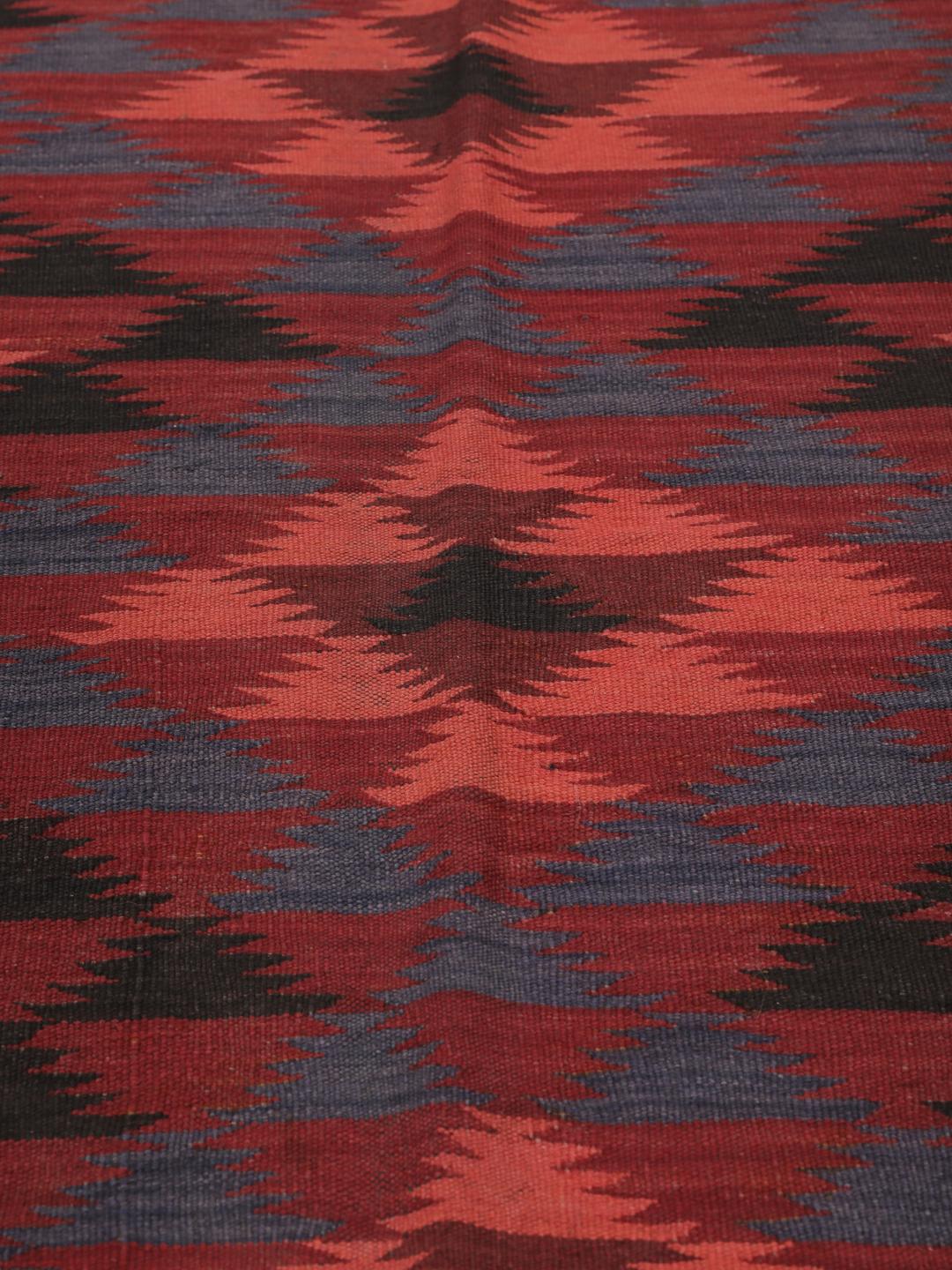 Tapis kelim afghan tissé à la main avec des motifs géométriques dans des tons rouges et sombres.