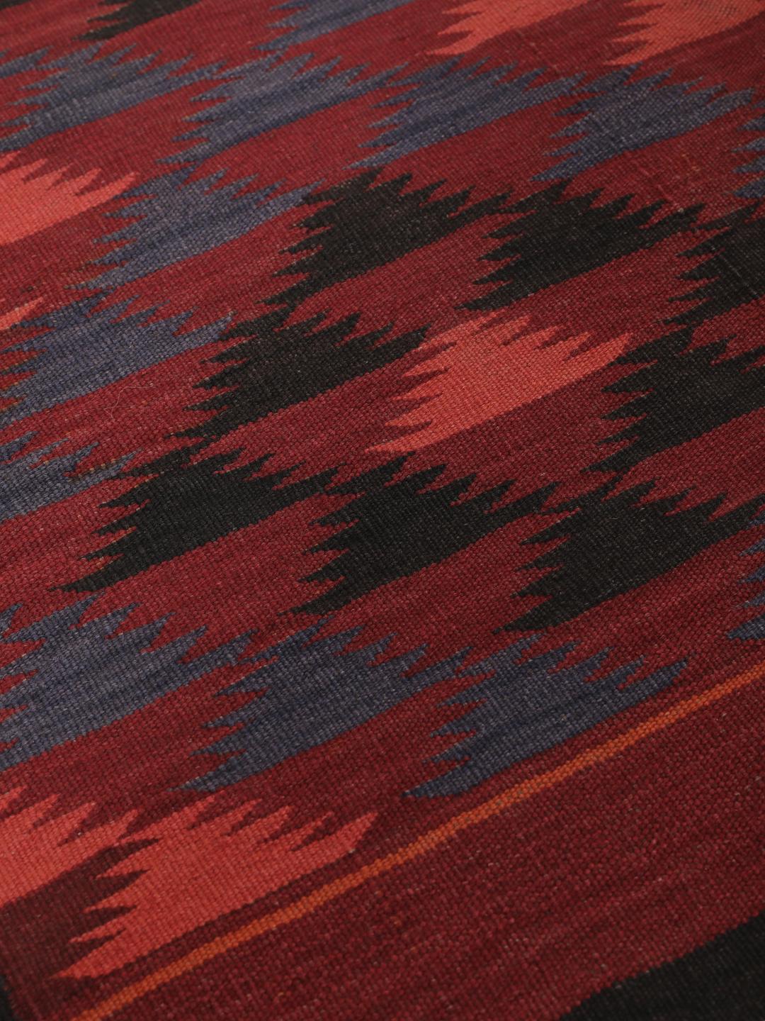 Tapis kelim afghan tissé à la main avec des motifs géométriques dans des tons rouges et sombres.