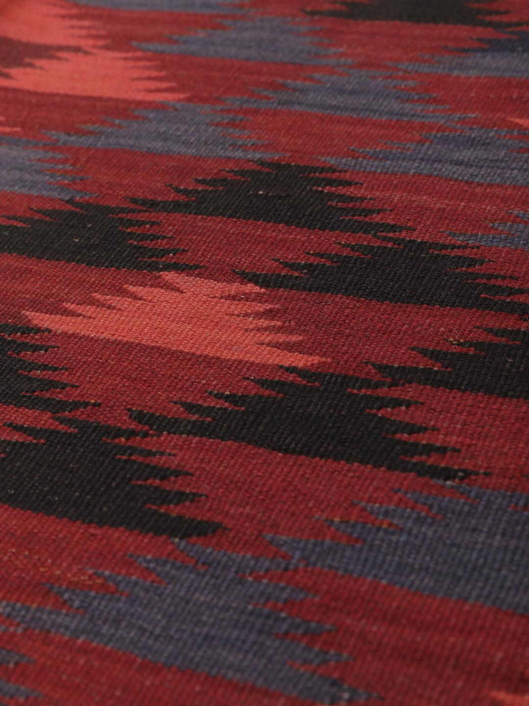 Tapis kelim afghan tissé à la main avec des motifs géométriques dans des tons rouges et sombres.