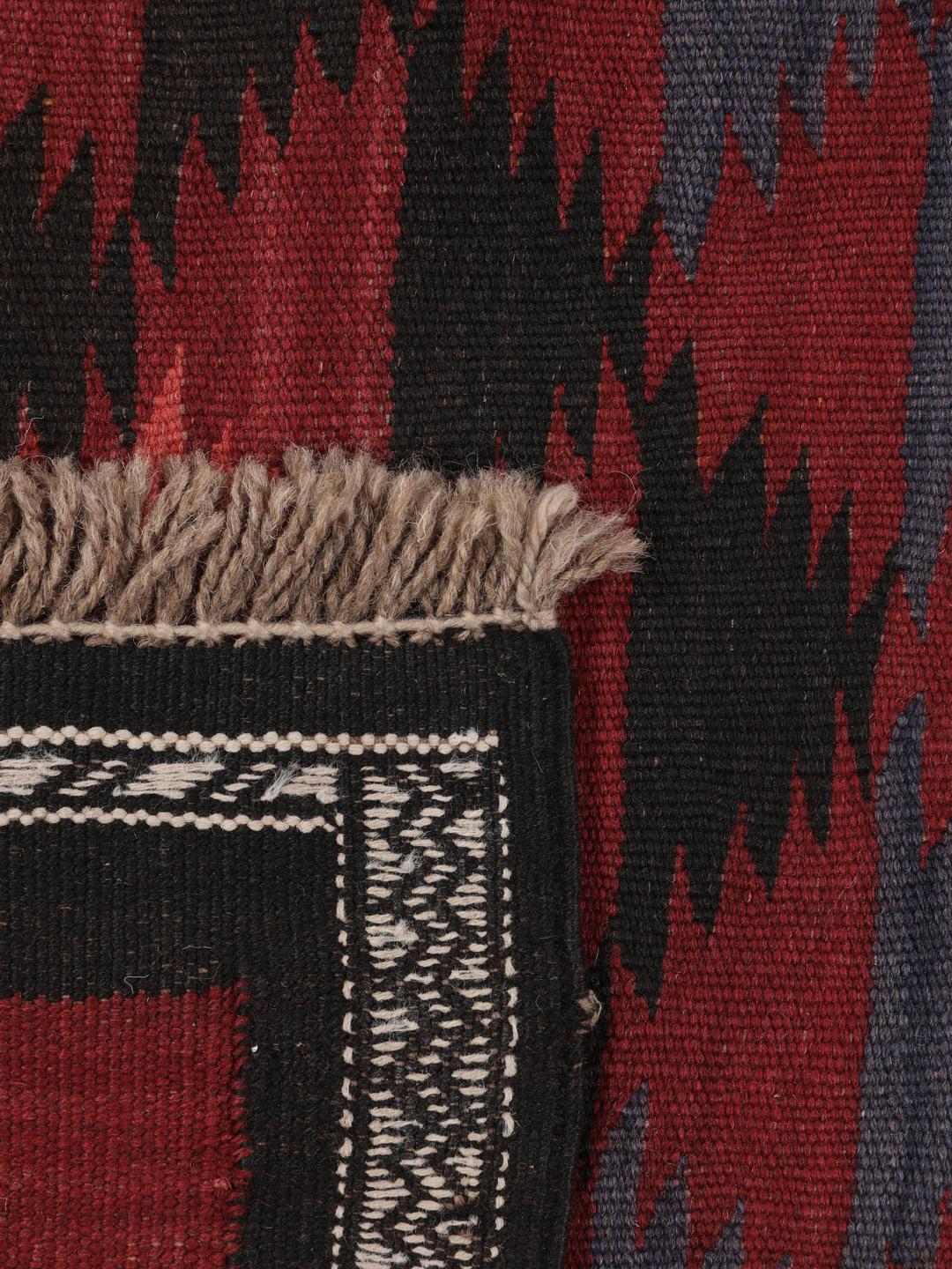 Tapis kelim afghan tissé à la main avec des motifs géométriques dans des tons rouges et sombres.