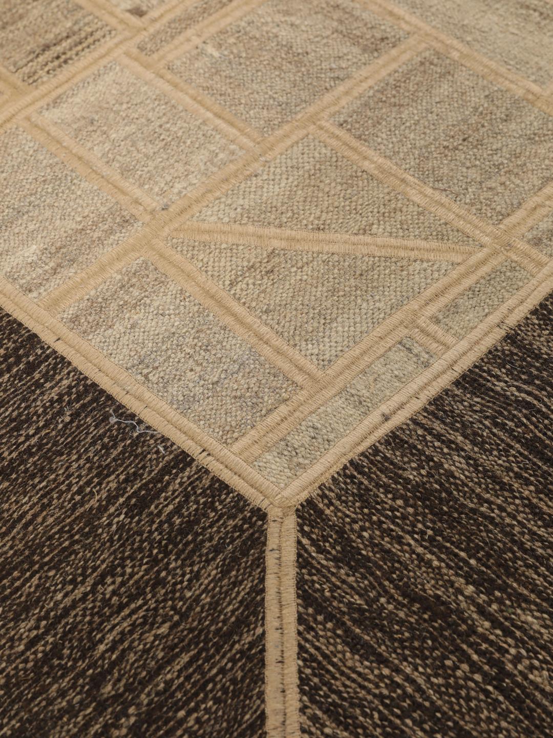 Un tapis patchwork rectangulaire avec des motifs géométriques en beige et marron, tissé à la main au Moyen-Orient.