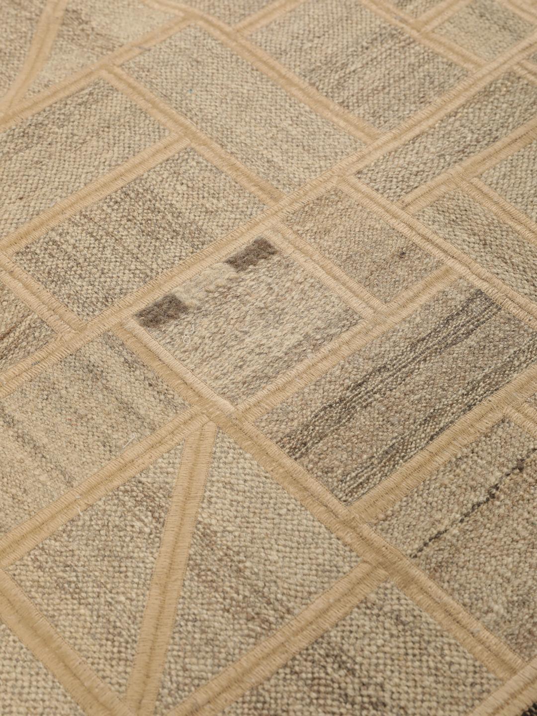 Un tapis patchwork rectangulaire avec des motifs géométriques en beige et marron, tissé à la main au Moyen-Orient.