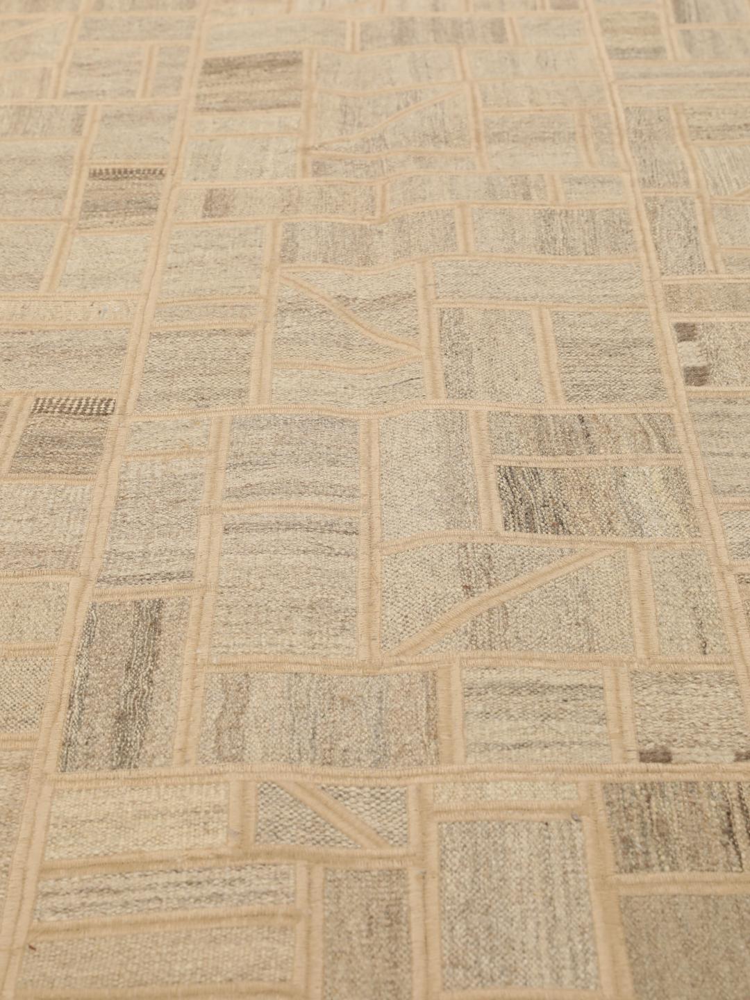 Un tapis patchwork rectangulaire avec des motifs géométriques en beige et marron, tissé à la main au Moyen-Orient.