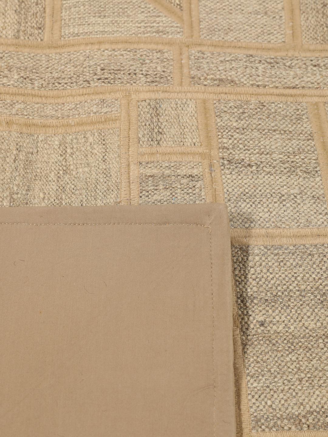 Un tapis patchwork rectangulaire avec des motifs géométriques en beige et marron, tissé à la main au Moyen-Orient.