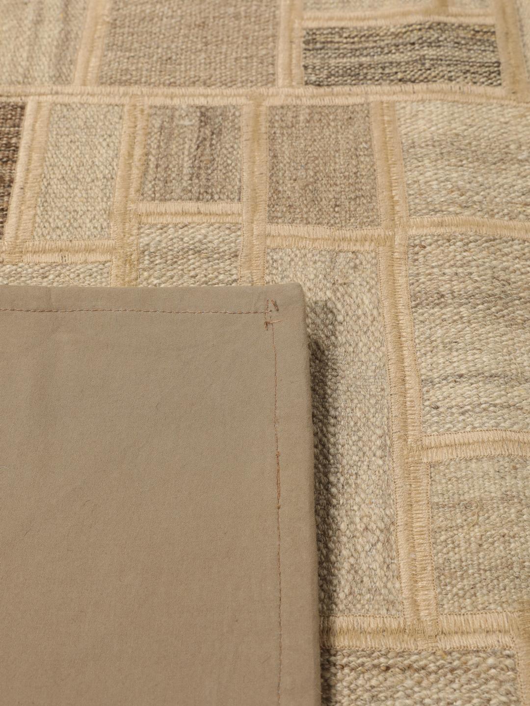 Een uniek rechthoekig patchwork tapijt met geometrische patronen in beige- en bruintinten.