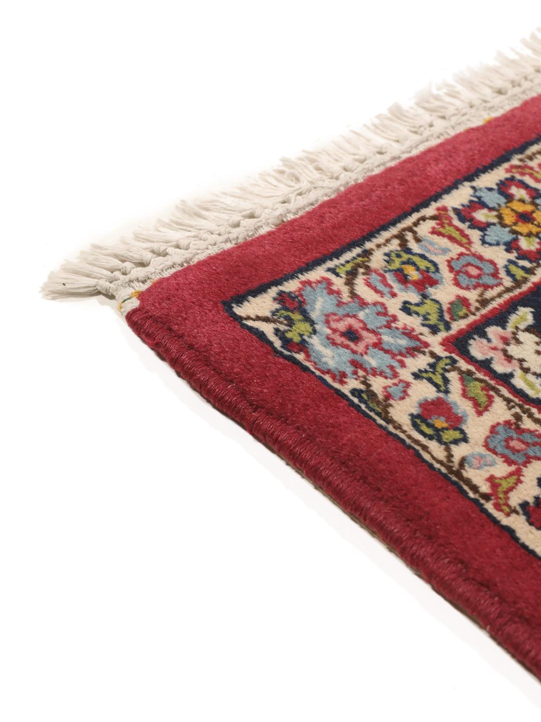 A hand-knotted Kerman rug with a floral medallion design in red and dark tones.