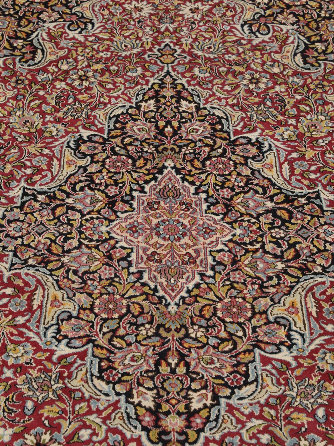 A hand-knotted Kerman rug with a floral medallion design in red and dark tones.