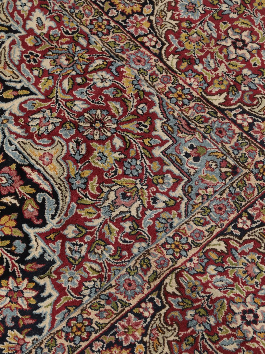 A hand-knotted Kerman rug with a floral medallion design in red and dark tones.