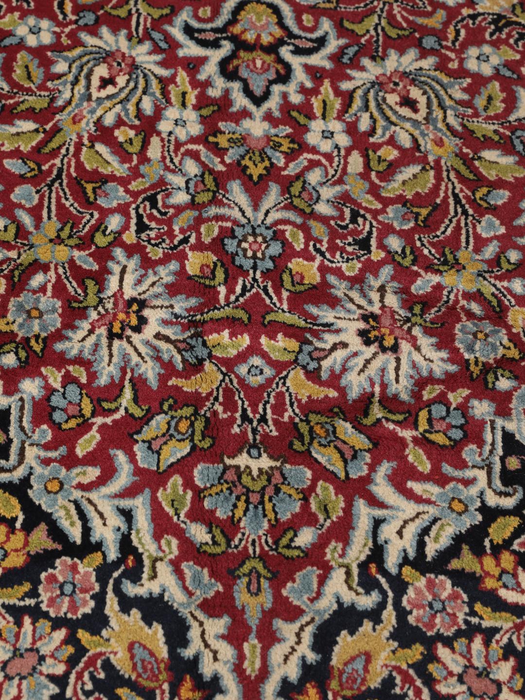 A hand-knotted Kerman rug with a floral medallion design in red and dark tones.