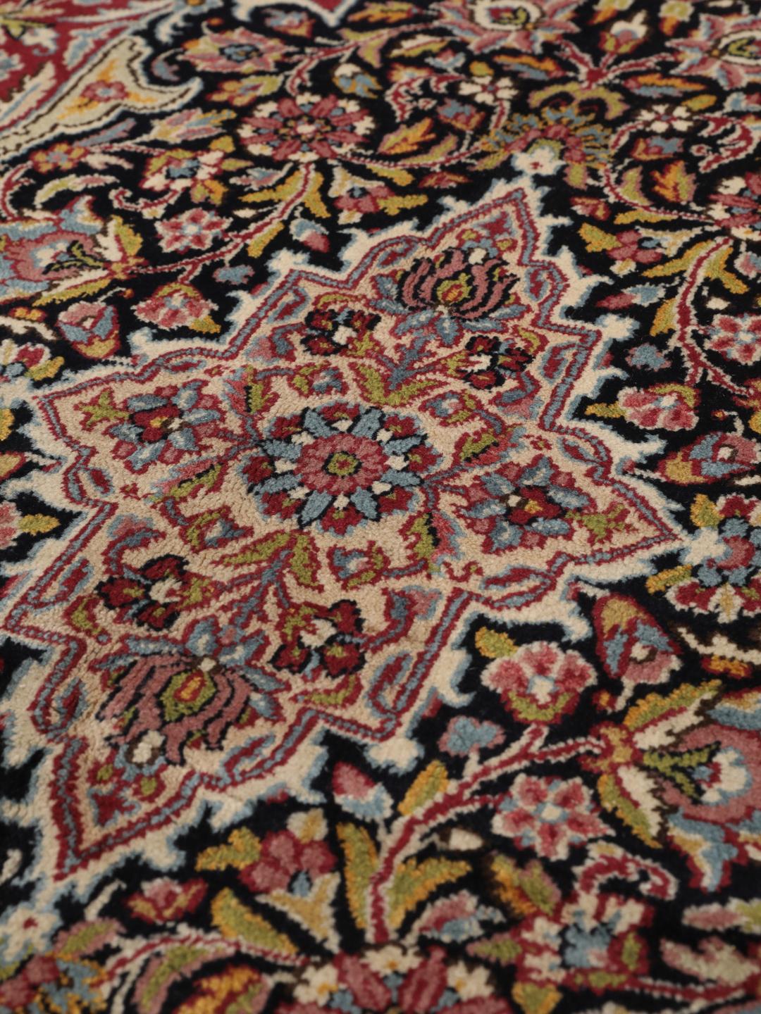 A hand-knotted Kerman rug with a floral medallion design in red and dark tones.