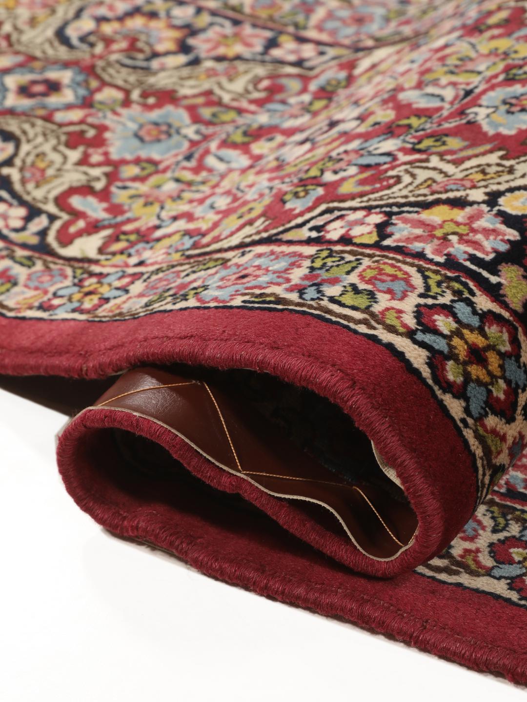 A hand-knotted Kerman rug with a floral medallion design in red and dark tones.