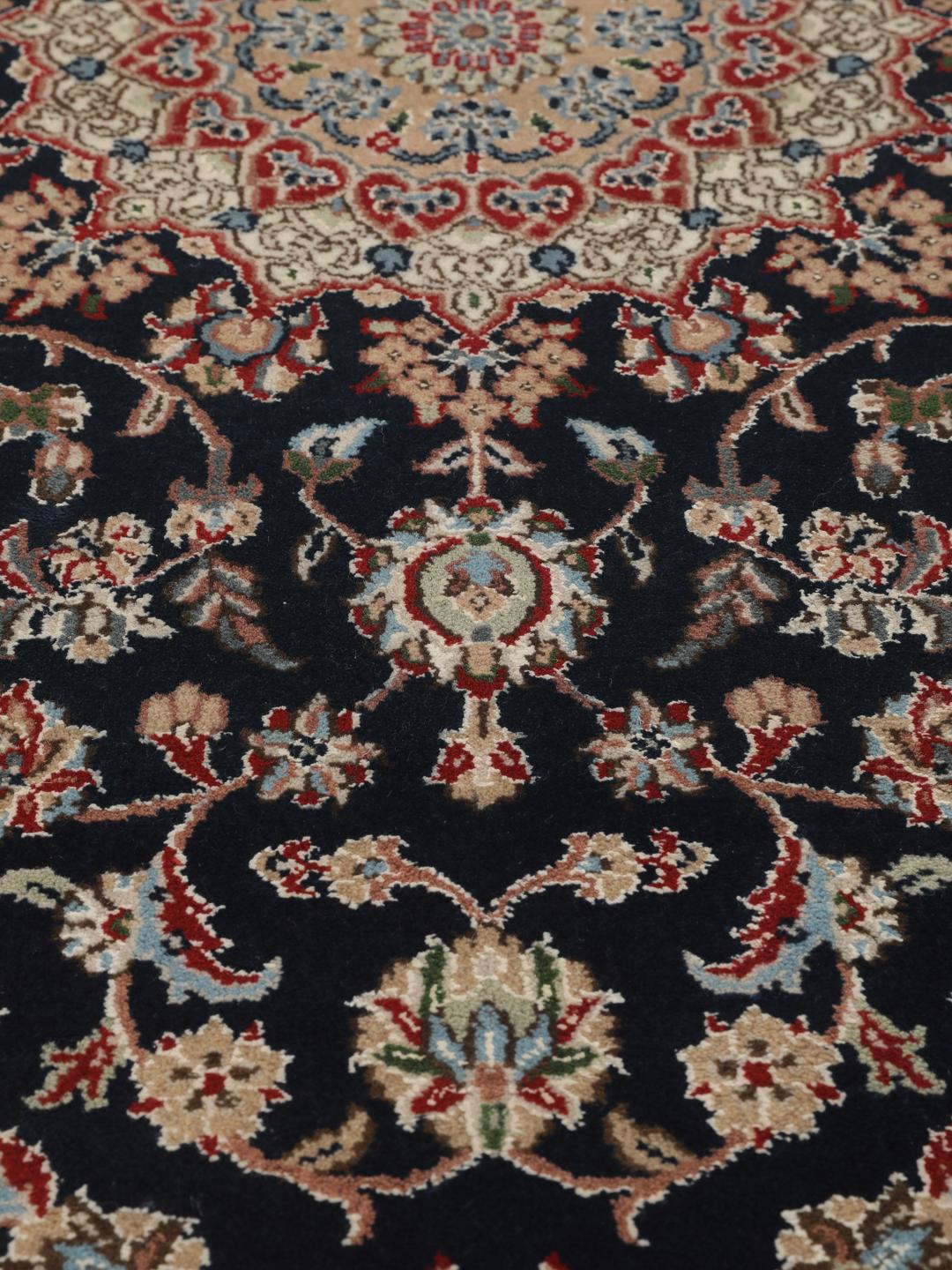 Un tapis rectangulaire Nain Indo présentant un champ bleu foncé avec un médaillon floral central et des bordures complexes, noué à la main en Inde.