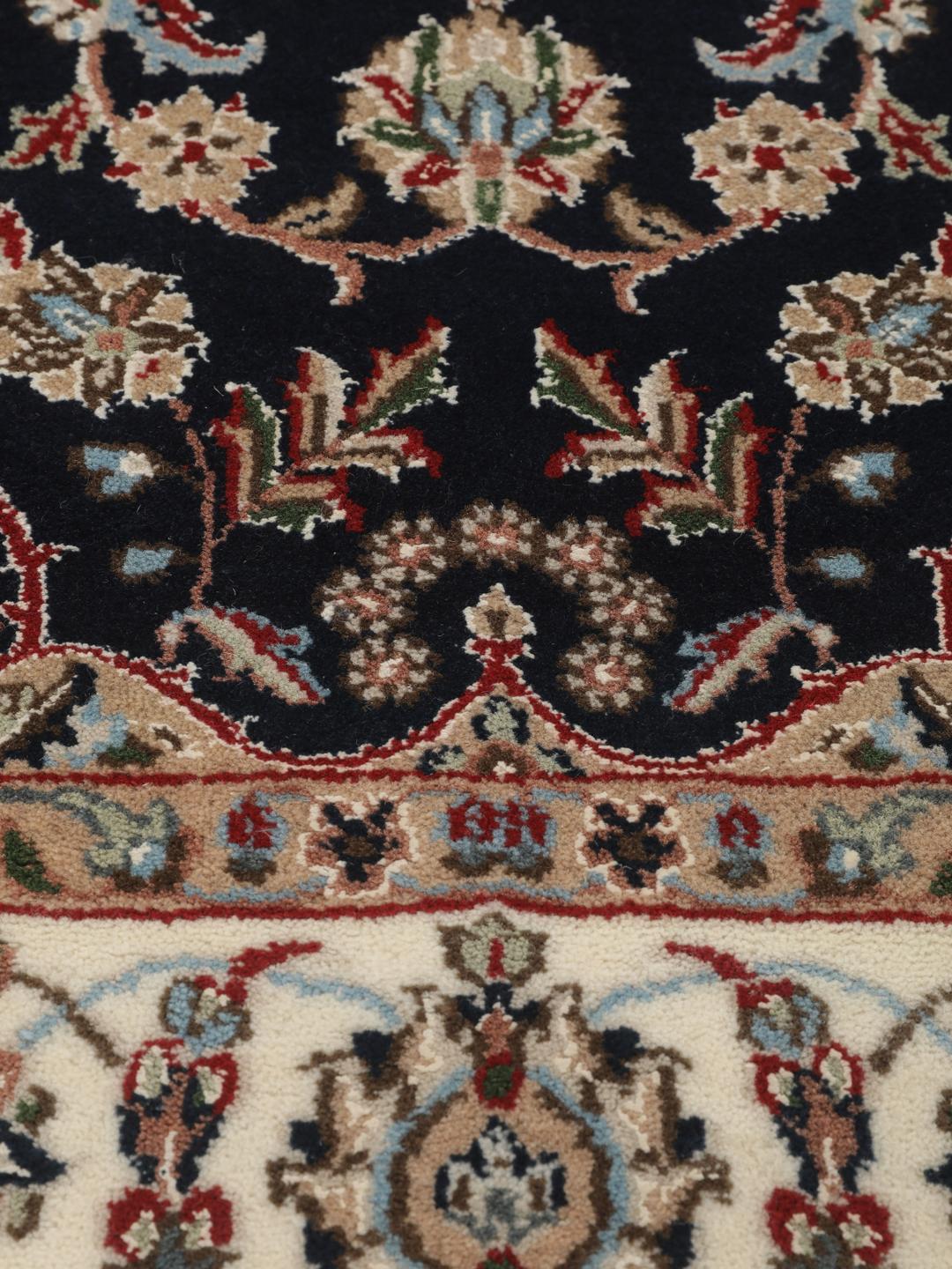 Un tapis rectangulaire Nain Indo présentant un champ bleu foncé avec un médaillon floral central et des bordures complexes, noué à la main en Inde.