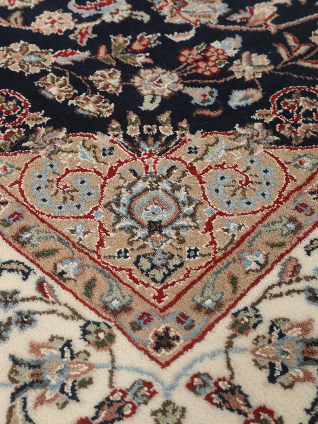 Un tapis rectangulaire Nain Indo présentant un champ bleu foncé avec un médaillon floral central et des bordures complexes, noué à la main en Inde.