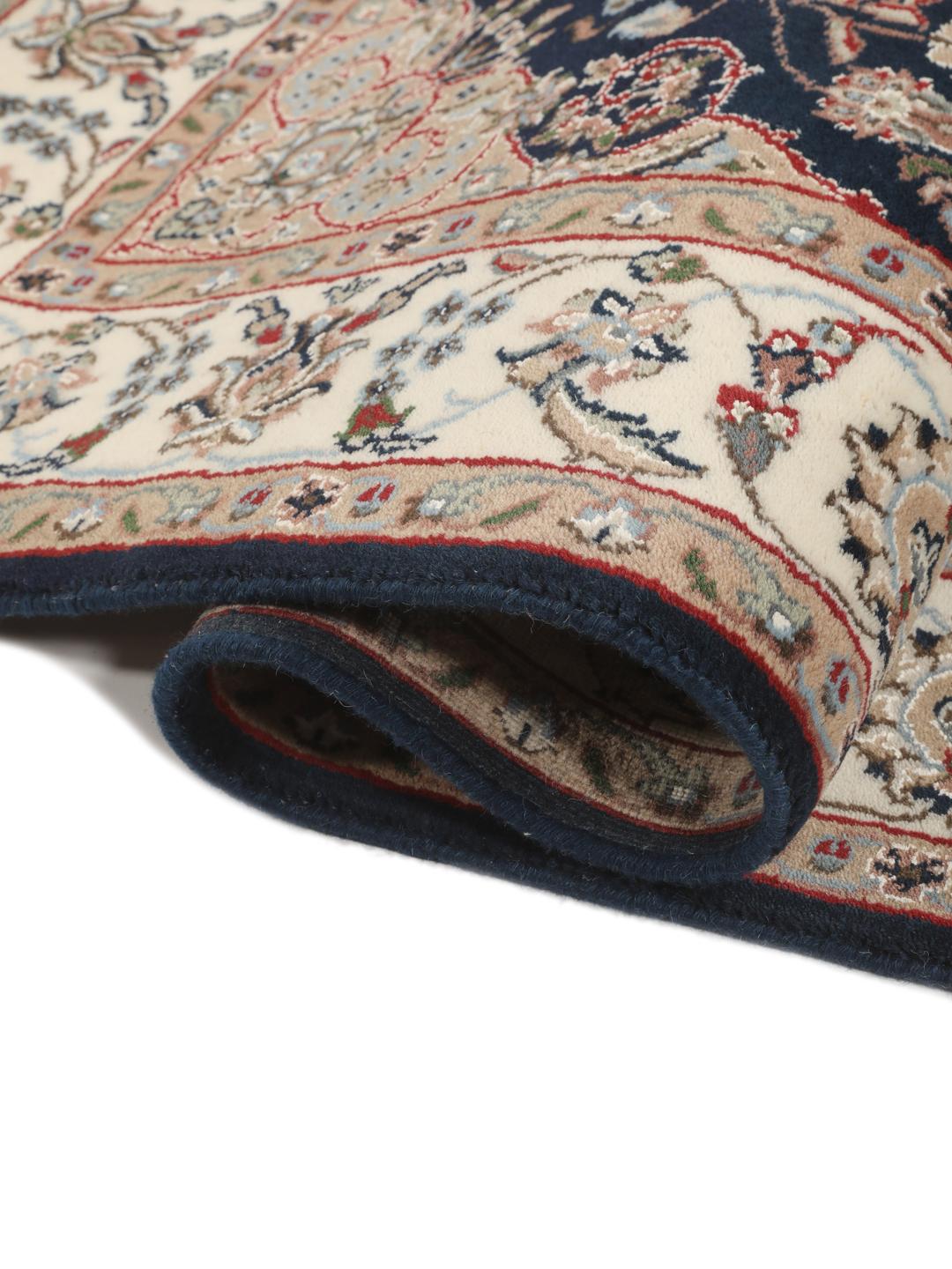 Un tapis rectangulaire Nain Indo présentant un champ bleu foncé avec un médaillon floral central et des bordures complexes, noué à la main en Inde.