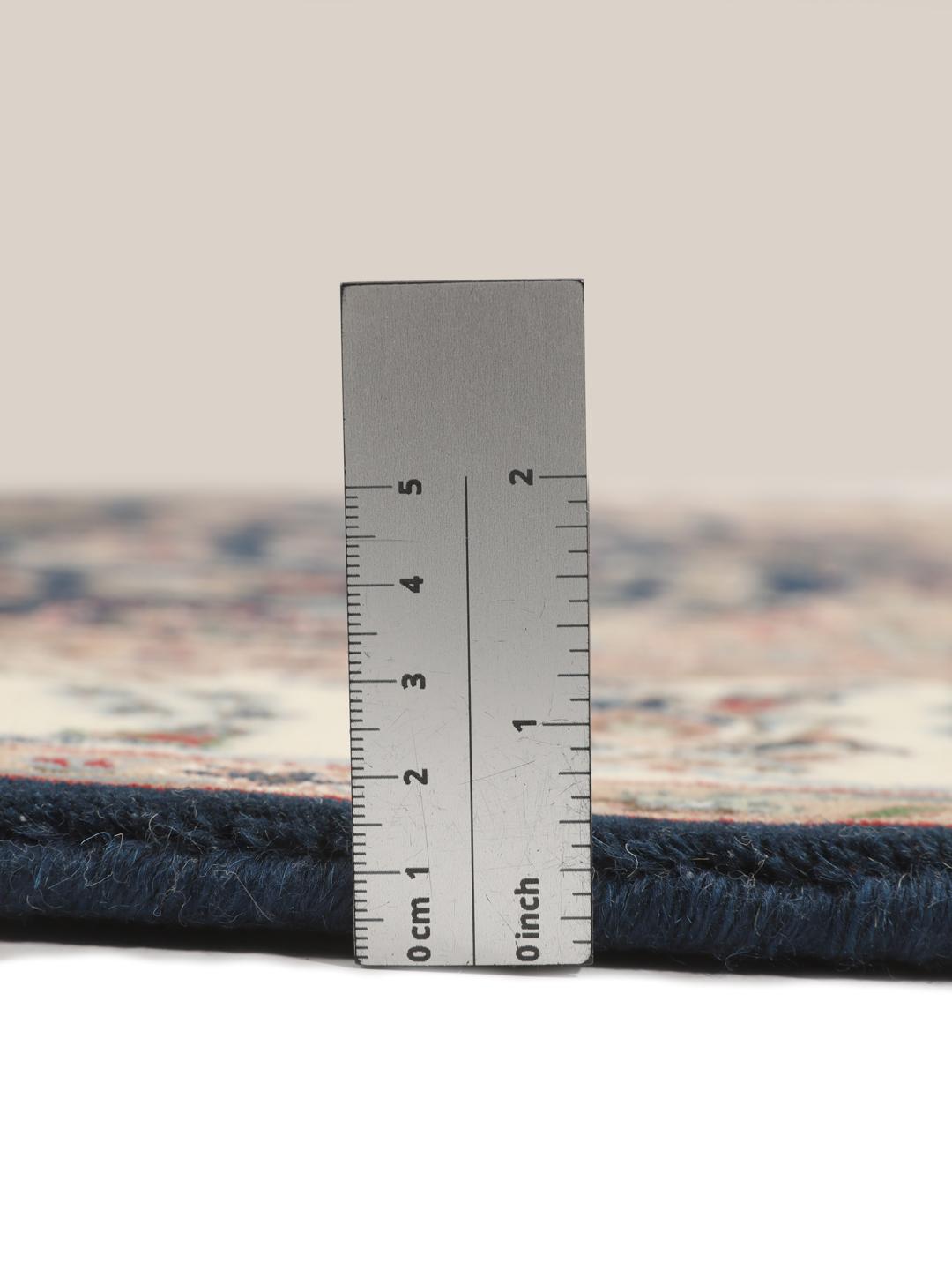Un tapis rectangulaire Nain Indo présentant un champ bleu foncé avec un médaillon floral central et des bordures complexes, noué à la main en Inde.