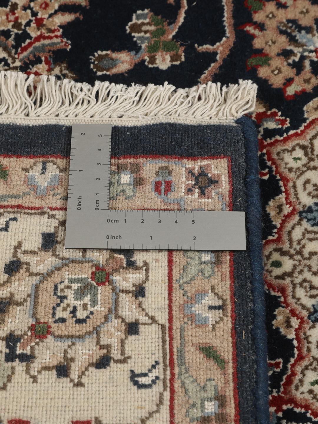 Un tapis rectangulaire Nain Indo présentant un champ bleu foncé avec un médaillon floral central et des bordures complexes, noué à la main en Inde.