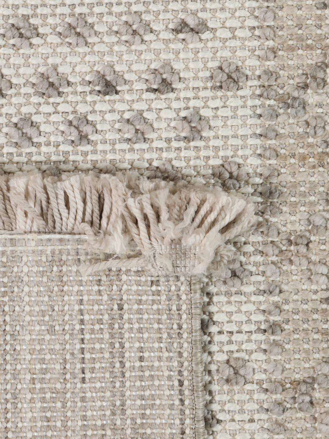 Beige tæppe med høj- og lavluvet tekstur og frynsedetaljer