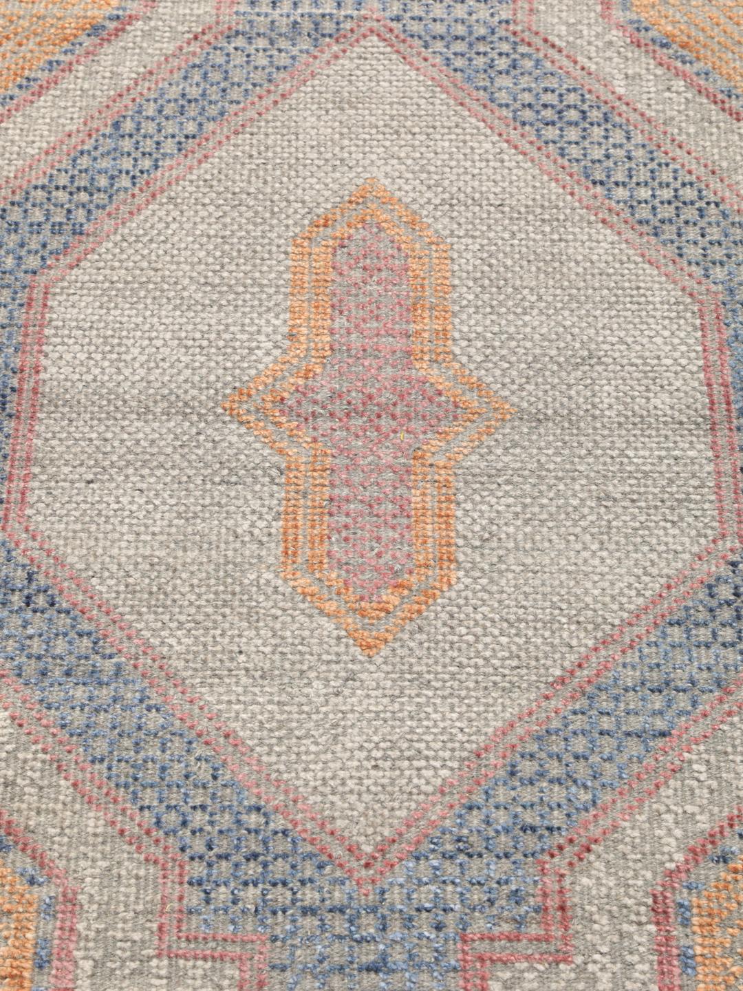 Modern handgeknoopt tapijt uit India met geometrische patronen in blauwe, roze en beige tinten.