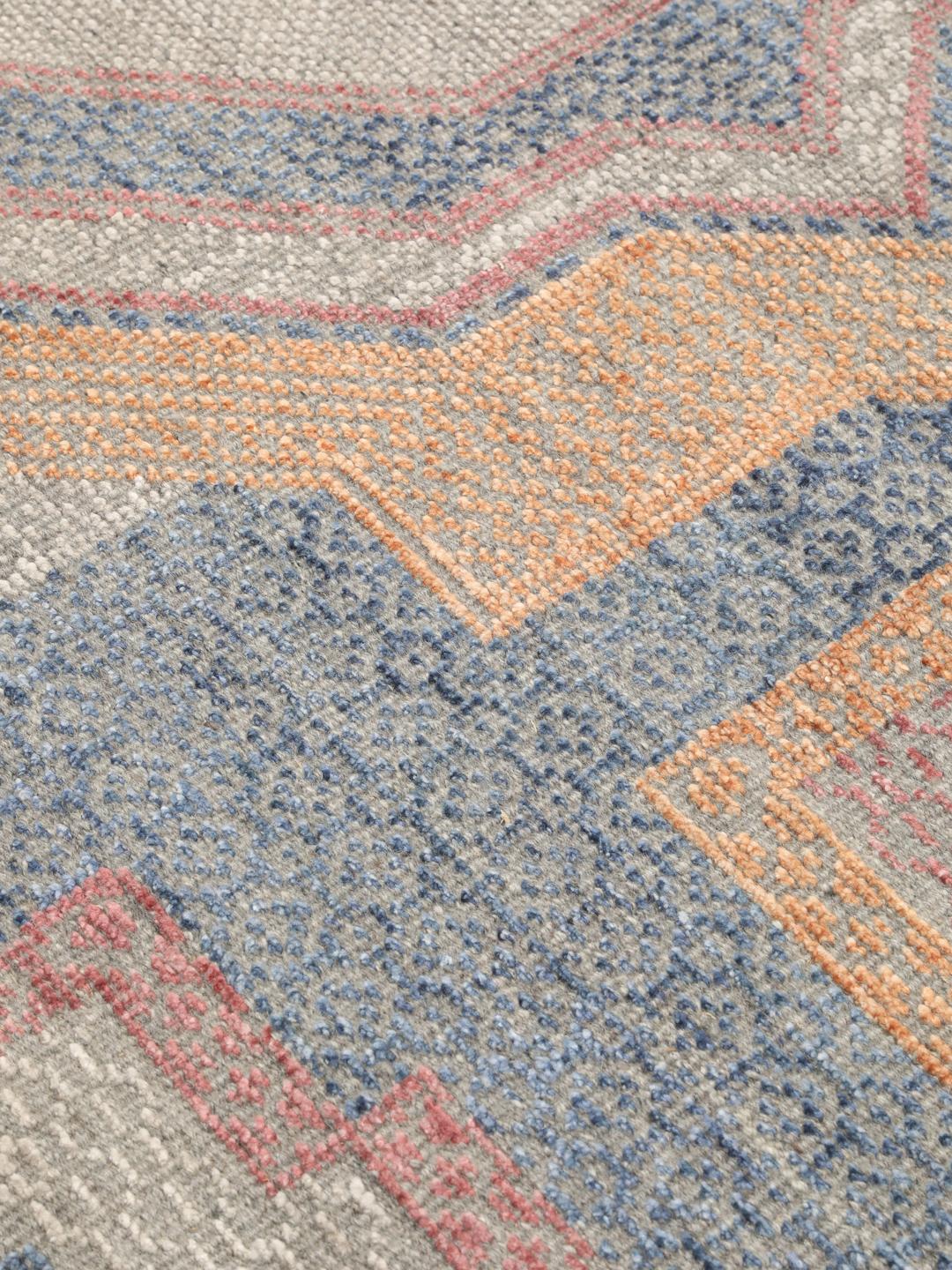 Modern handgeknoopt tapijt uit India met geometrische patronen in blauwe, roze en beige tinten.