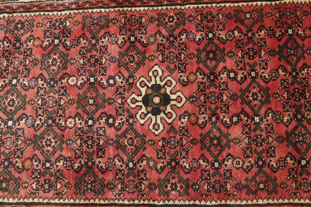 A long, hand-knotted Hosseinabad runner rug with a red field and geometric motifs.