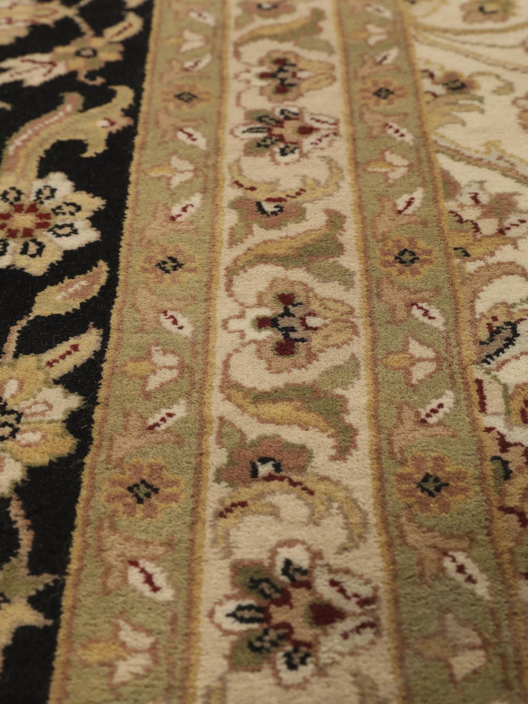 A large, hand-knotted Sarough rug from India featuring an intricate floral design on a beige field with a black border.