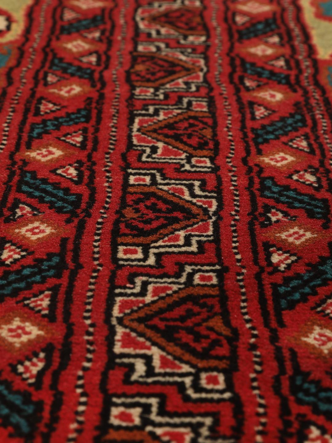 A hand-knotted Turkaman rug from the Middle East with a vibrant red and multicoloured geometric design.