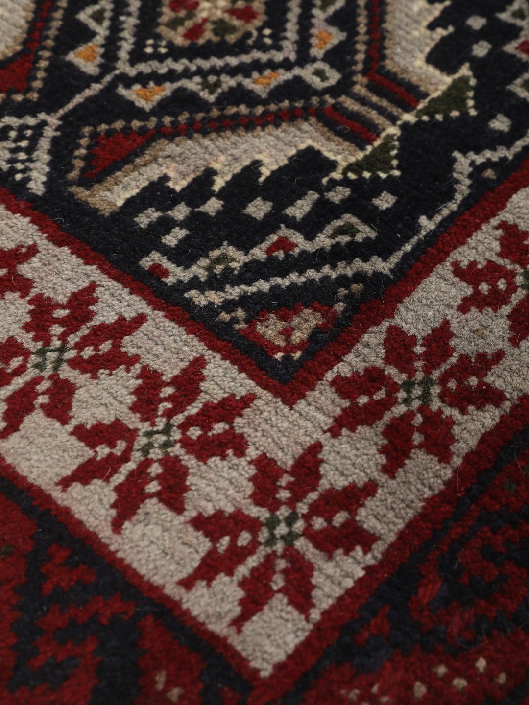 Et håndknyttet Baluch-tæppe fra Mellemøsten med en mørkeblå bund og geometriske røde og hvide mønstre.