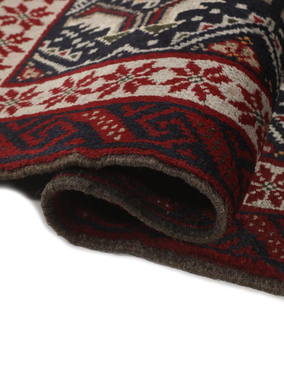 Et håndknyttet Baluch-tæppe fra Mellemøsten med en mørkeblå bund og geometriske røde og hvide mønstre.