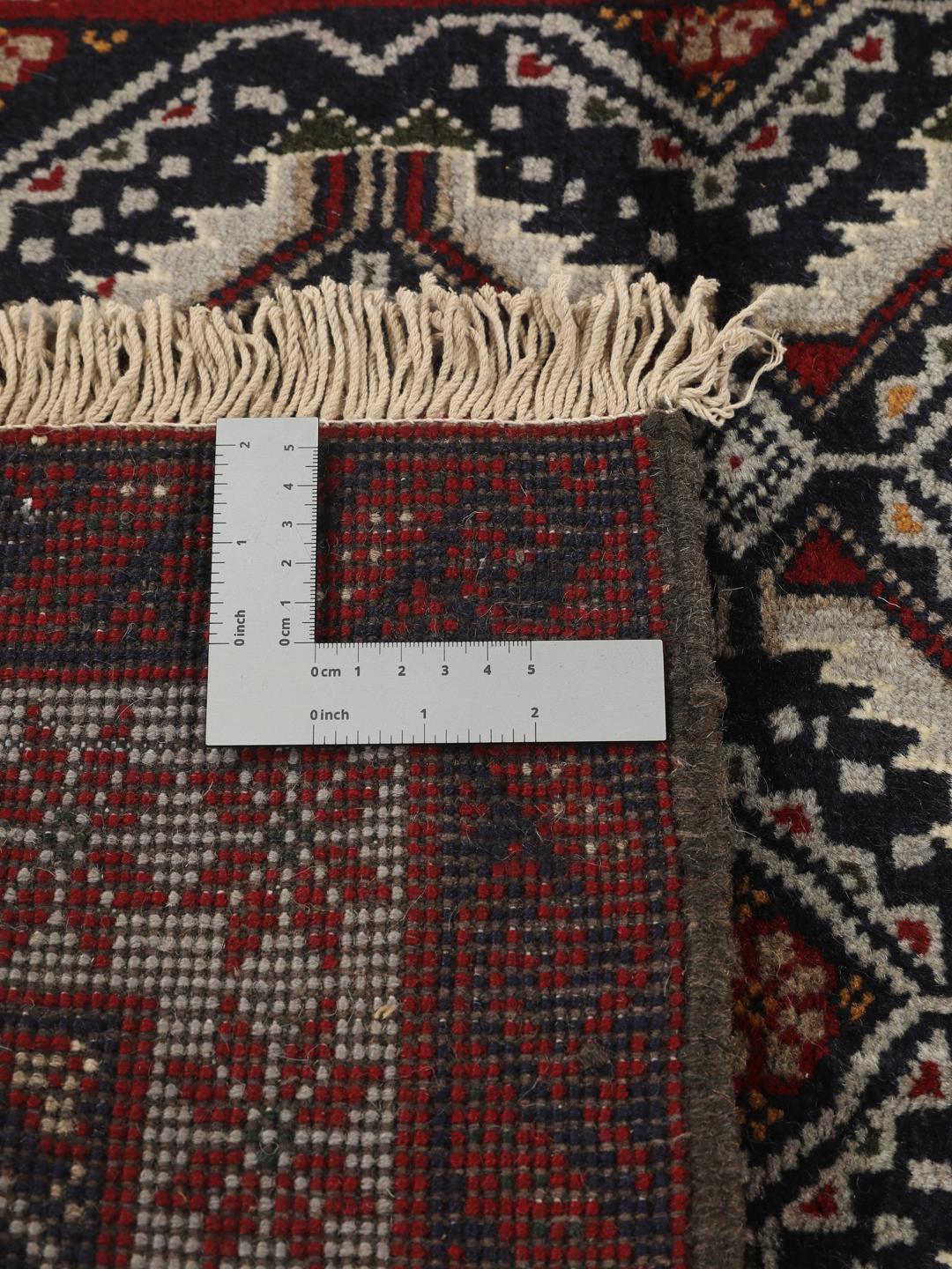 Et håndknyttet Baluch-tæppe fra Mellemøsten med en mørkeblå bund og geometriske røde og hvide mønstre.