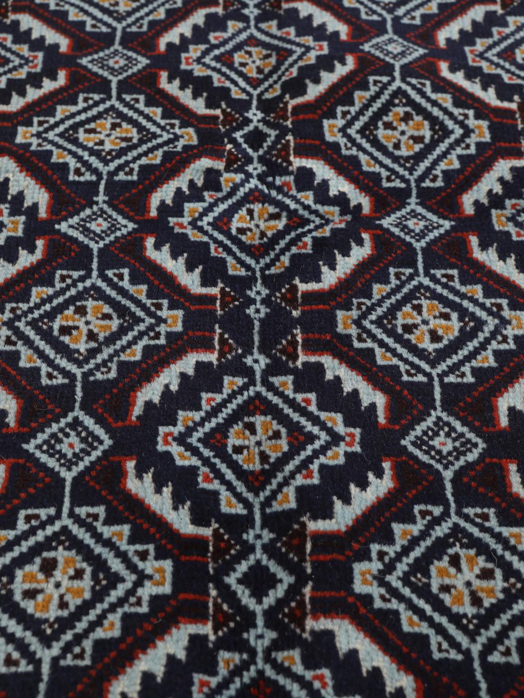 Hand-knotted Baluch rug with geometric motifs in dark-red and black tones.