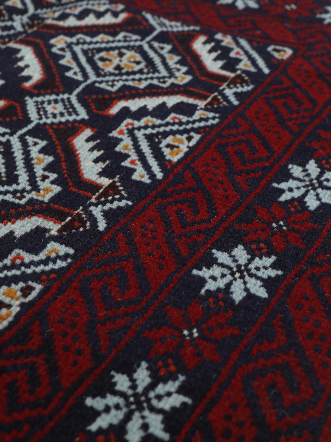 Hand-knotted Baluch rug with geometric motifs in dark-red and black tones.