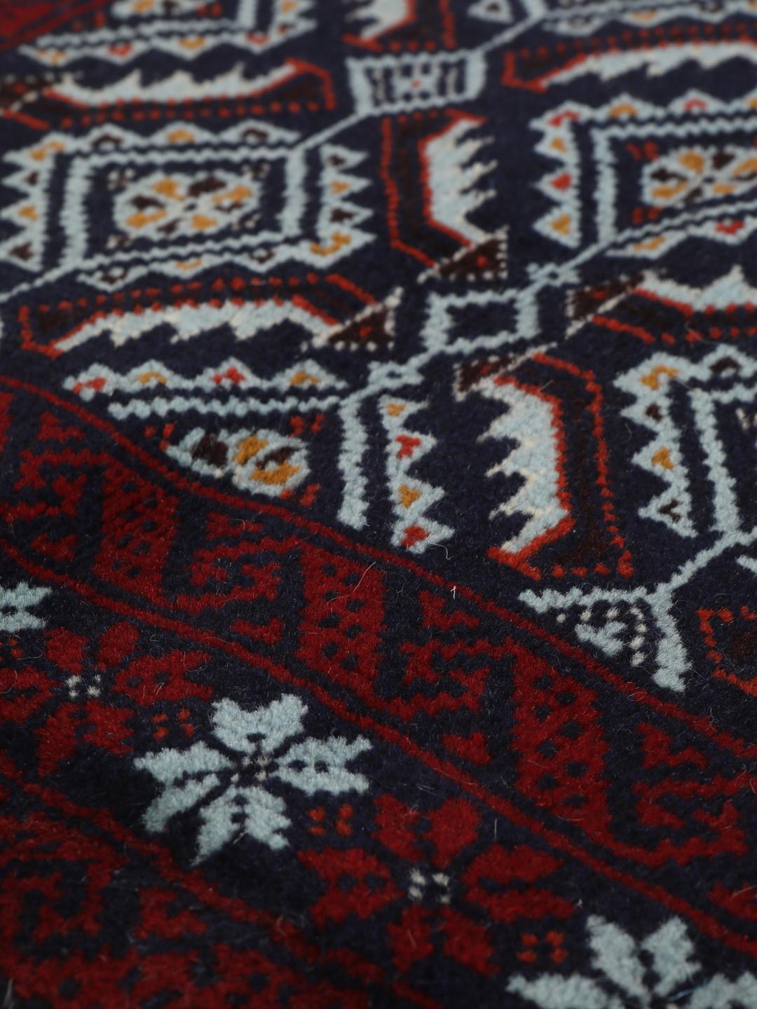 Hand-knotted Baluch rug with geometric motifs in dark-red and black tones.