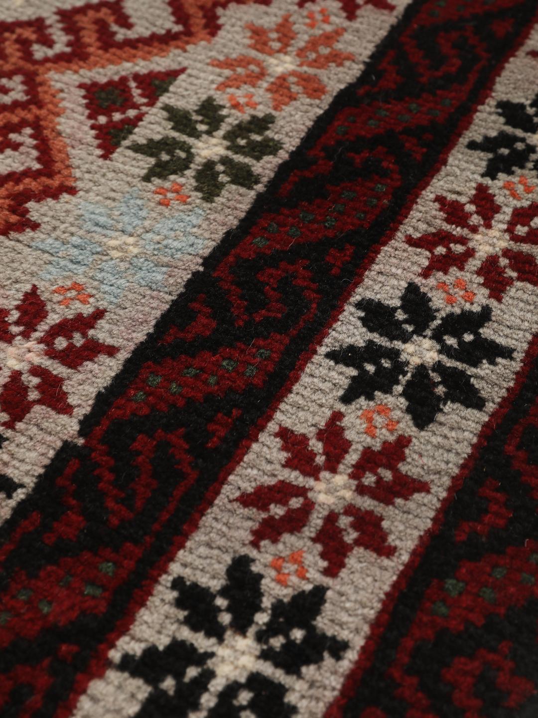 Et håndknyttet Baluch-tæppe fra Mellemøsten med røde og flerfarvede geometriske mønstre.
