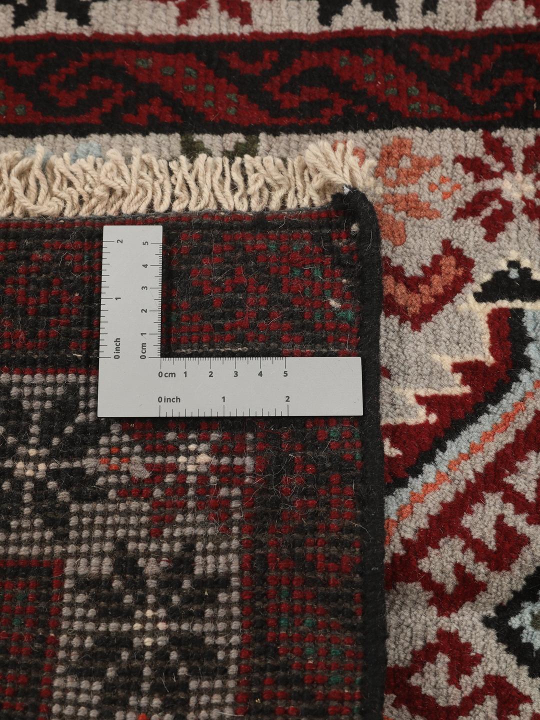 Et håndknyttet Baluch-tæppe fra Mellemøsten med røde og flerfarvede geometriske mønstre.