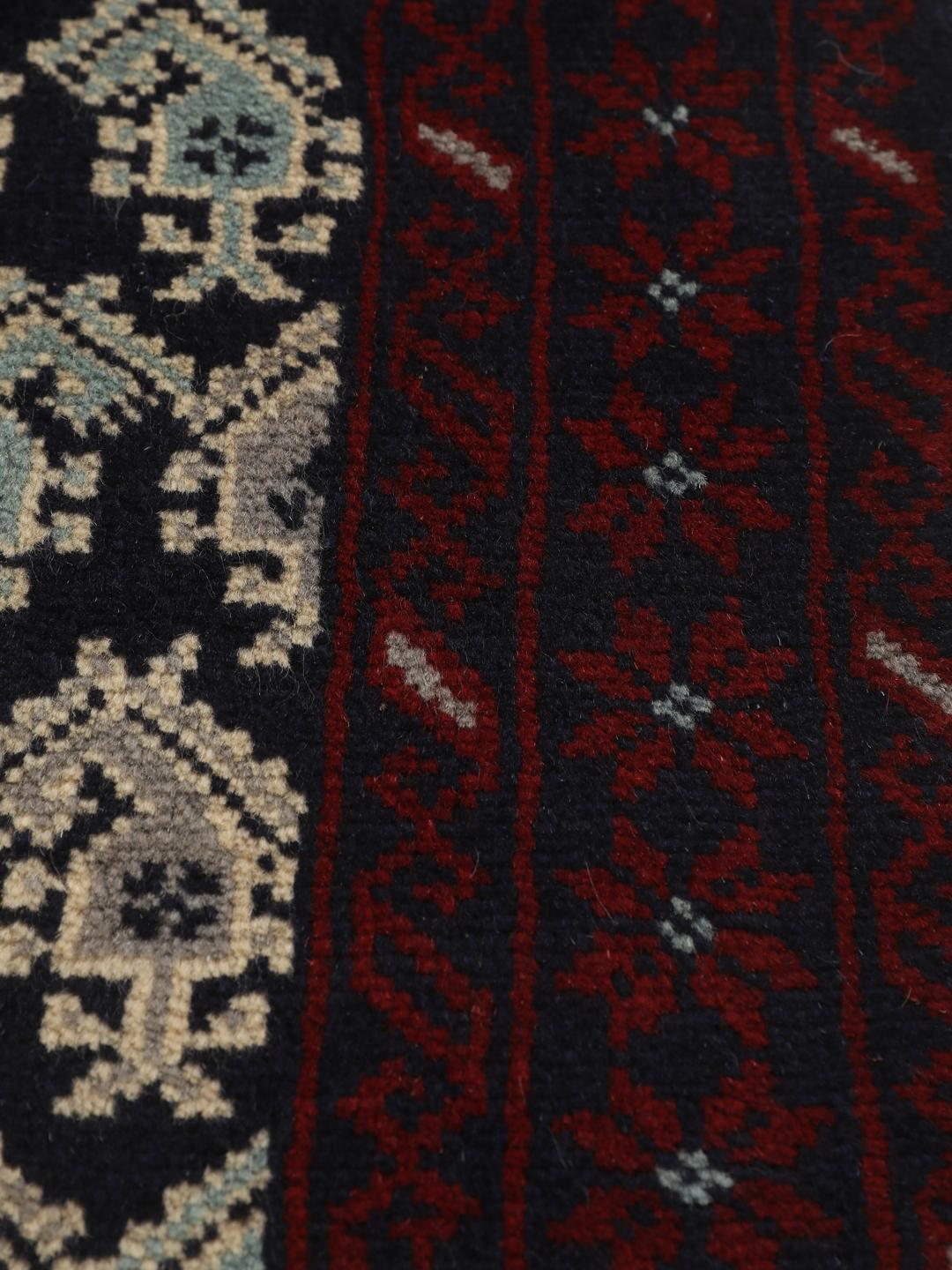Handgeknoopt Baluch-tapijt met ingewikkelde geometrische motieven in donkerblauw en rood.
