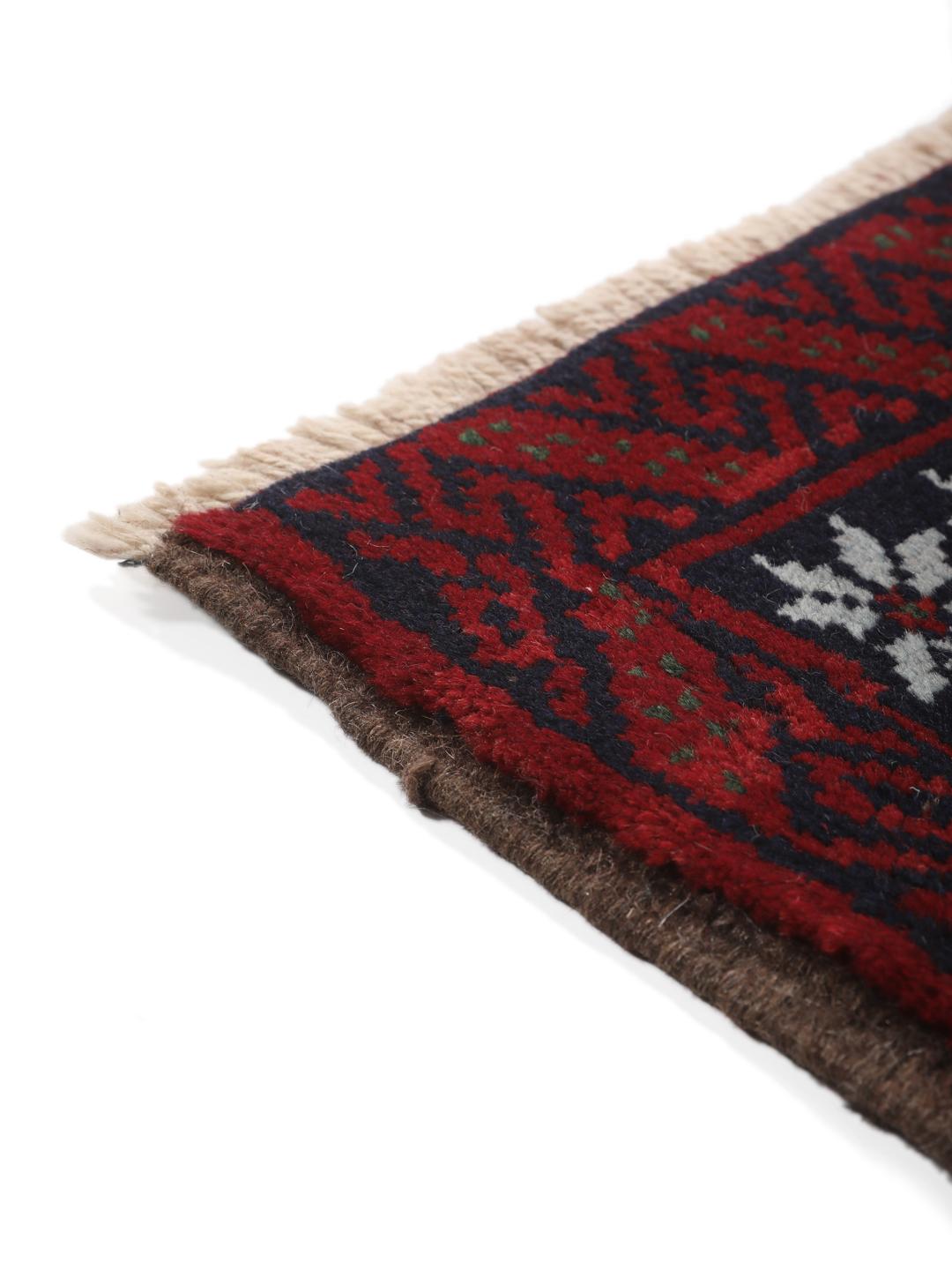 A hand-knotted Baluch rug from the Middle East featuring a dark-red and black geometric pattern.