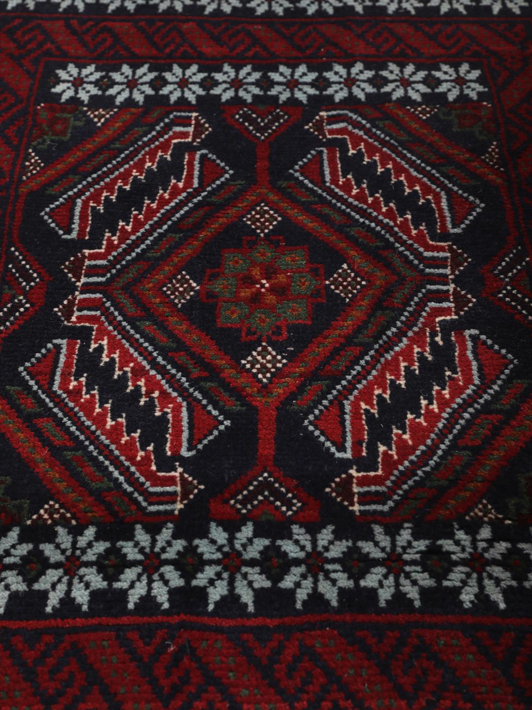 A hand-knotted Baluch rug from the Middle East featuring a dark-red and black geometric pattern.