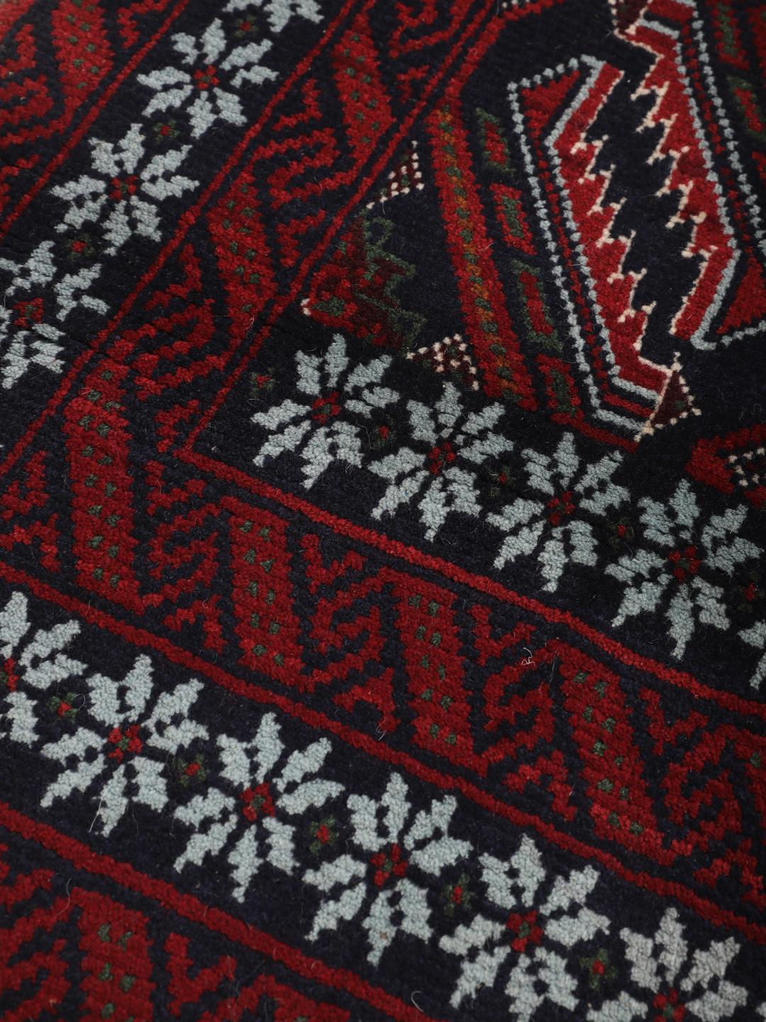 A hand-knotted Baluch rug from the Middle East featuring a dark-red and black geometric pattern.